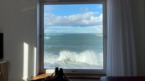 A room with a large window overlooking the sea, a television on the left, and a wooden table in the foreground. - Generals Yard (Eyemouth)