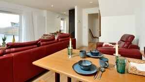 A modern living room with a red leather sofa, a wooden dining table with blue ceramic dinnerware, and a view of the sea through large windows. - Generals Yard (Eyemouth)