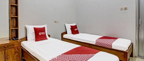 A hotel room with two single beds, each with white bedding and red pillows, a wooden nightstand, and a mirror.