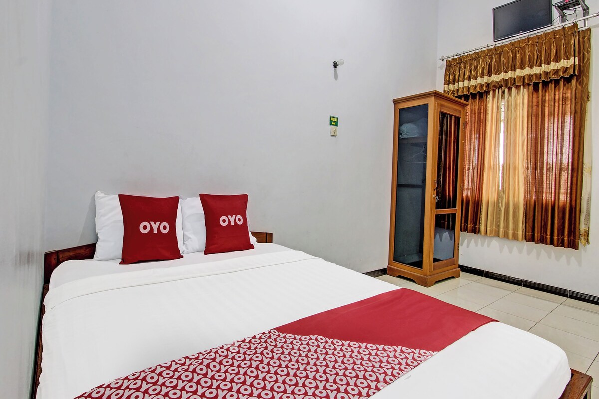 Ein Hotelzimmer mit einem großen Bett, rot-weiß gestreifter Bettwäsche, einem Holzschrank und einem Vorhang mit goldenem Muster.