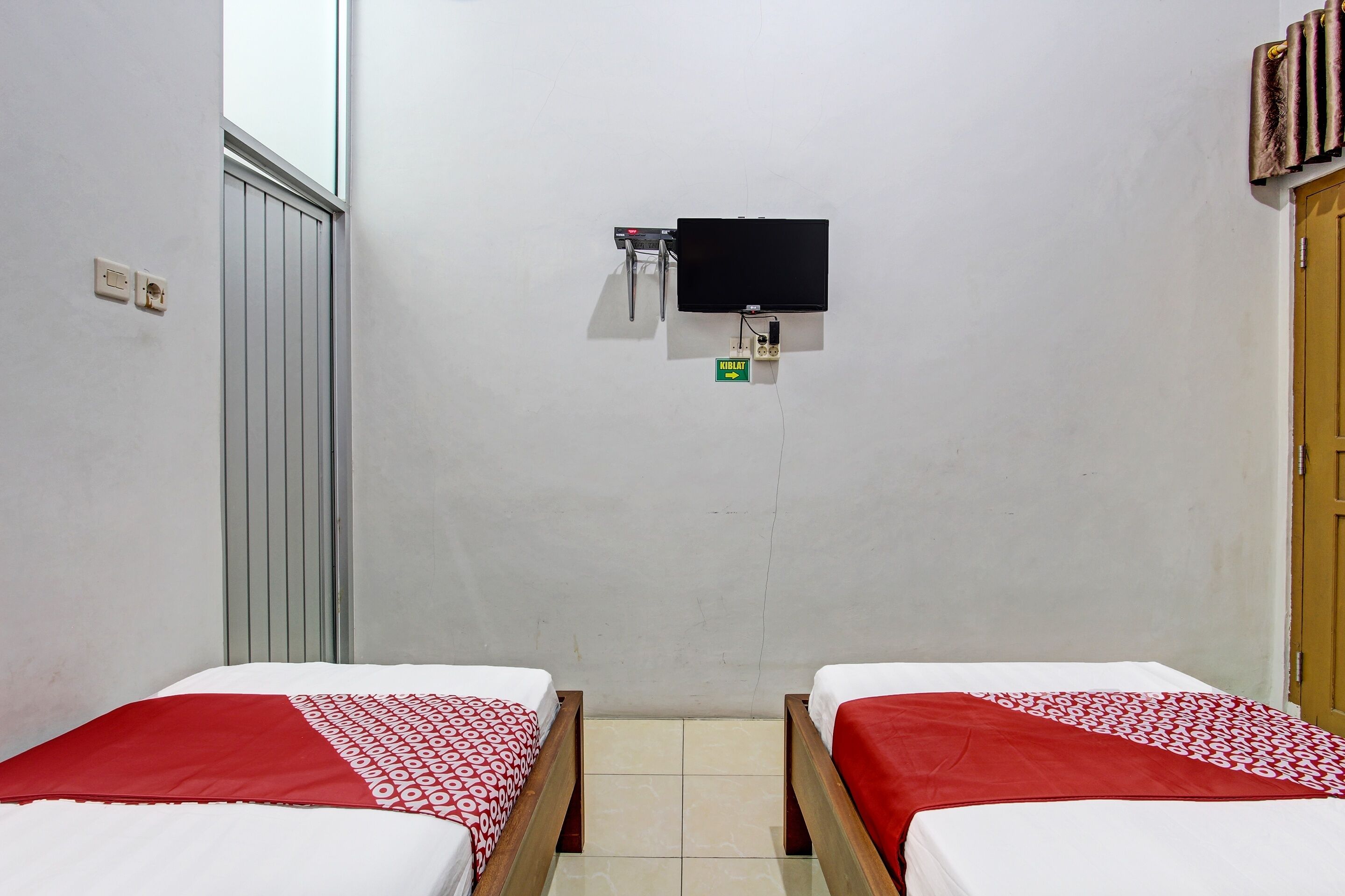 Una habitación con dos camas, televisor instalado en la pared y una puerta.