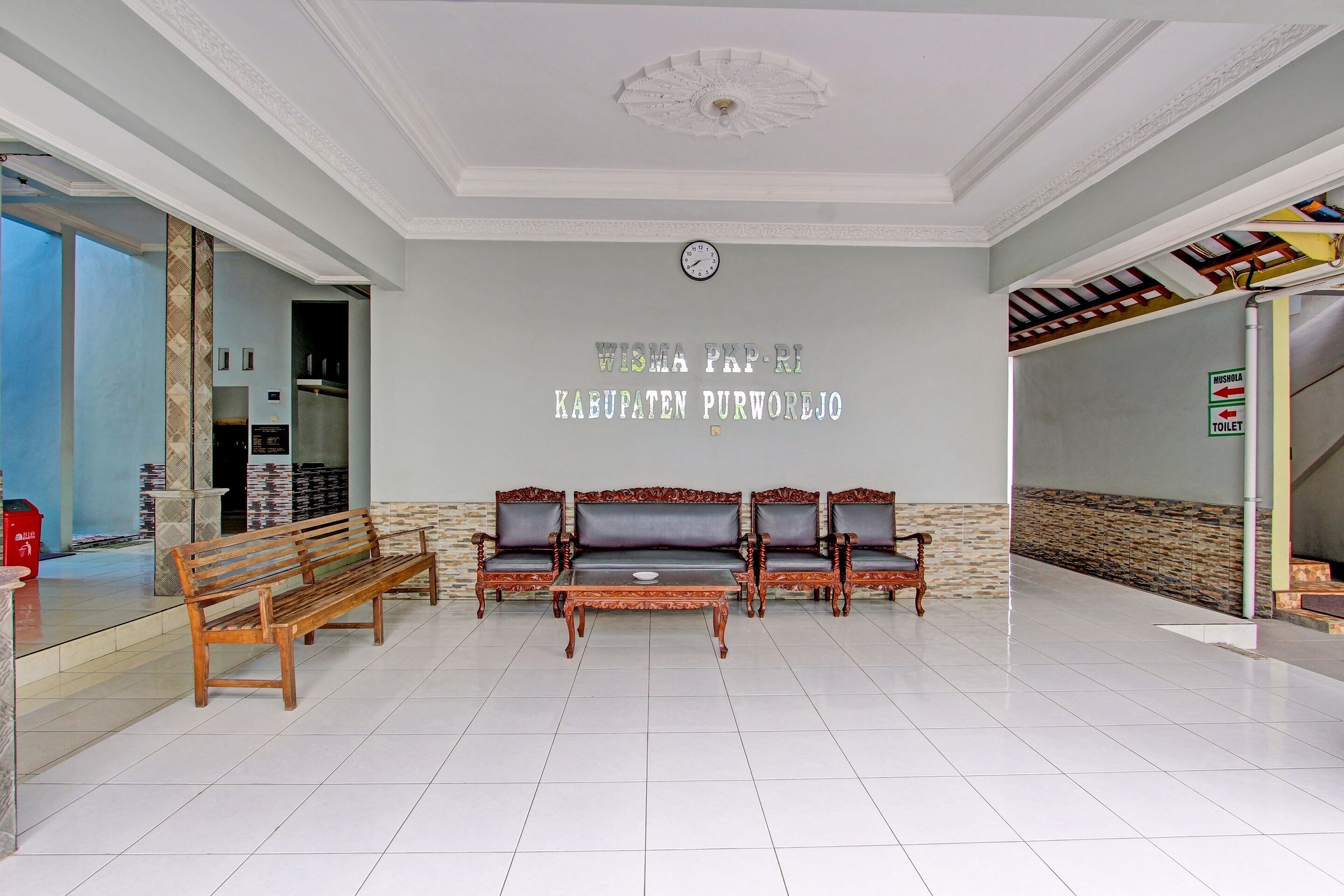 A lobby with a reception desk, a wooden bench, a sofa set, and a clock on the wall.