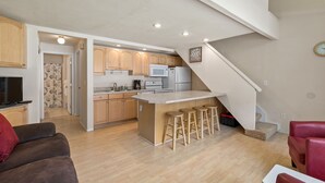 Eine moderne Küche mit Holzschränken, einer zentralen Kochinsel mit Hockern und einer Treppe, die in eine andere Ebene führt.