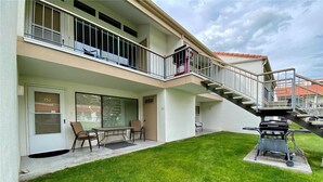 A two-story building with a balcony, a barbecue grill, and a small patio area with chairs and a table.