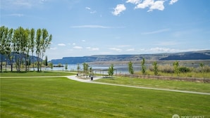 A grassy area with a walking path, a small pavilion, and a body of water in the background.