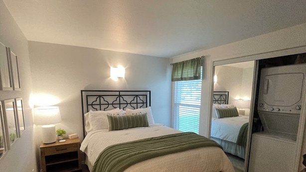 A bedroom with a bed, bedside table, lamp, and a mirror.