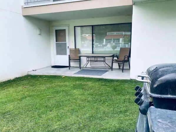A patio with a table and chairs, a sliding glass door, and a small lawn area.