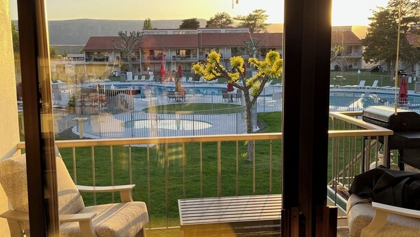 A balcony with a view of a swimming pool, lounge chairs, and a tree with yellow flowers. - #16 Condo by large pool & shuttle to Gorge Amp-Book Separately (Quincy)