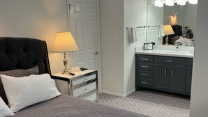 A bedroom with a bed, bedside table, lamp, and a bathroom with a mirror, sink, and cabinets. - #16 Condo by large pool & shuttle to Gorge Amp-Book Separately (Quincy)