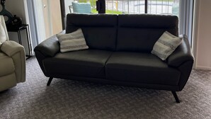 A living room with a dark leather sofa, a light-colored armchair, and a large sliding glass door leading to a pool area. - #16 Condo by large pool & shuttle to Gorge Amp-Book Separately (Quincy)