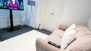 A living room with a flat-screen TV on a stand, a sofa with a remote control, a floor lamp, and a door. - Londwell - Luxury Knightsbridge Flat - Harrods (London)
