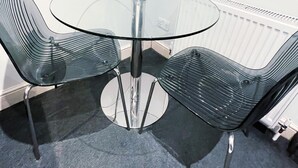 A round glass table with two metal chairs, a white radiator, and a grey carpeted floor. - Londwell - Luxury Knightsbridge Flat - Harrods (London)