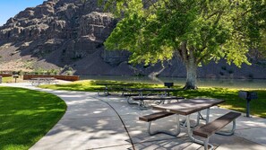 A park with picnic tables, benches, a grassy area, and a lake with mountains in the background.