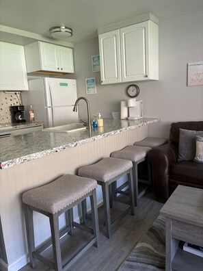 A kitchen with white cabinets, a stainless steel refrigerator, a coffee maker, and a clock on the wall.