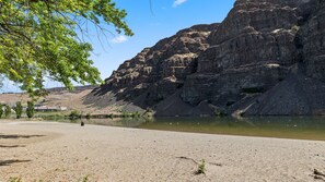 A river with rocky cliffs, a sandy beach, and sparse vegetation.