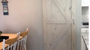 Uma área de refeições com mesa e cadeiras de madeira, uma porta corrediça tipo celeiro e uma placa fixada na parede.