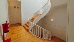 Una escalera de madera con balaustres blancos, un extintor y una puerta blanca al fondo.
