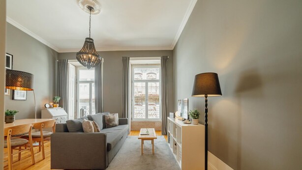 Una sala de estar moderna con un sofá gris, una mesa de comedor de madera y una araña.