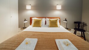 Una cama bien tendida con una colcha marrón a rayas, dos lámparas de noche y dos lámparas de pared.