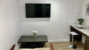 A modern kitchen with a flat-screen TV mounted on the wall, a dining table with chairs, and a bar area with a stool. - Minimalist Living 1BR In-Law AC Unit with Private Washer & Dryer (Hayward, California)