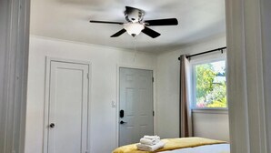A bedroom with a bed, a ceiling fan, two white doors, and a window with curtains. - Minimalist Living 1BR In-Law AC Unit with Private Washer & Dryer (Hayward, California)