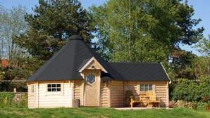 Une cabane en rondins avec un toit conique, une porte d’entrée et deux fenêtres.