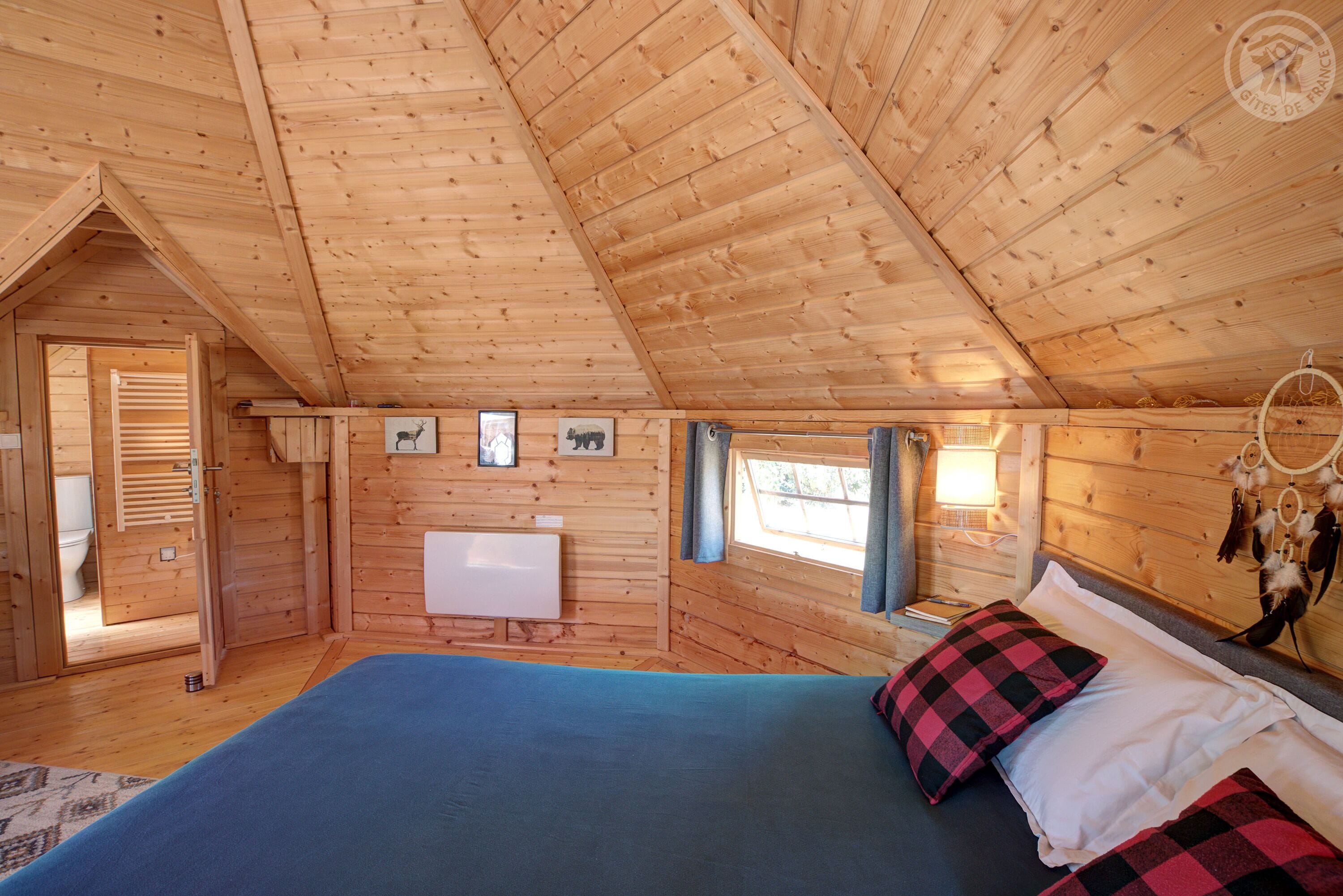 A wooden cabin bedroom with a bed, a radiator, and a window.