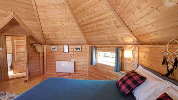 A wooden cabin bedroom with a bed, a radiator, and a window.