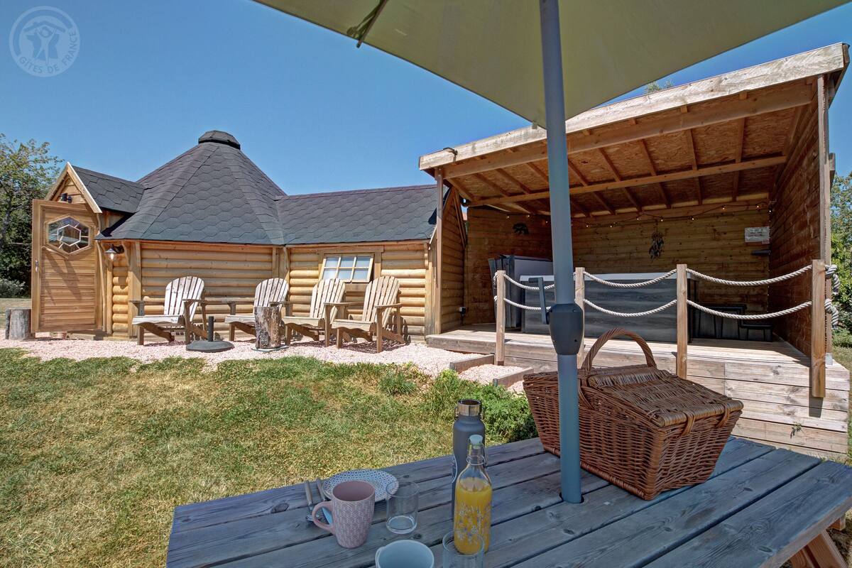 Eine Holzhütte mit überdachter Veranda, Sitzgelegenheit im Freien und einem Picknicktisch mit Flasche und Korb.