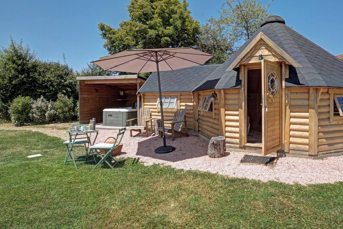 Eine kleine Holzhütte mit einer Terrassenfläche, einem Tisch und Stühlen sowie einem großen Sonnenschirm.