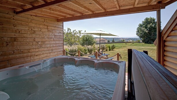 Une cabane en bois dotée d’un bain à remous et offrant une vue sur un paysage verdoyant.