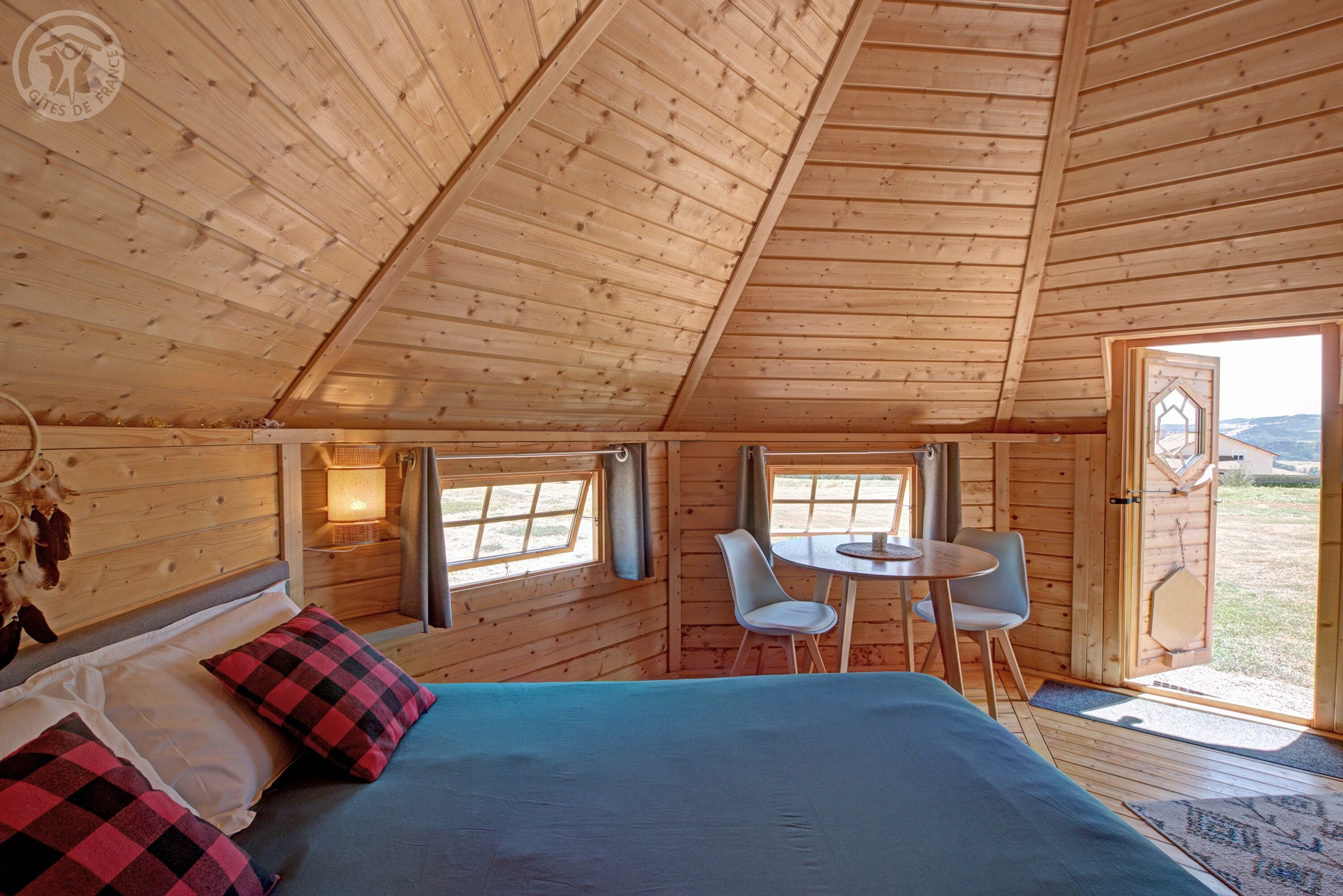 A wooden cabin with a bed, two chairs, a table, and a window.