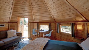 L’intérieur d’un chalet accueillant, avec un plafond en bois, un canapé, un lit, une table à manger avec des chaises et une fenêtre.