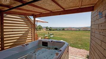 A wooden cabin with a hot tub, a covered patio, and a view of the countryside.