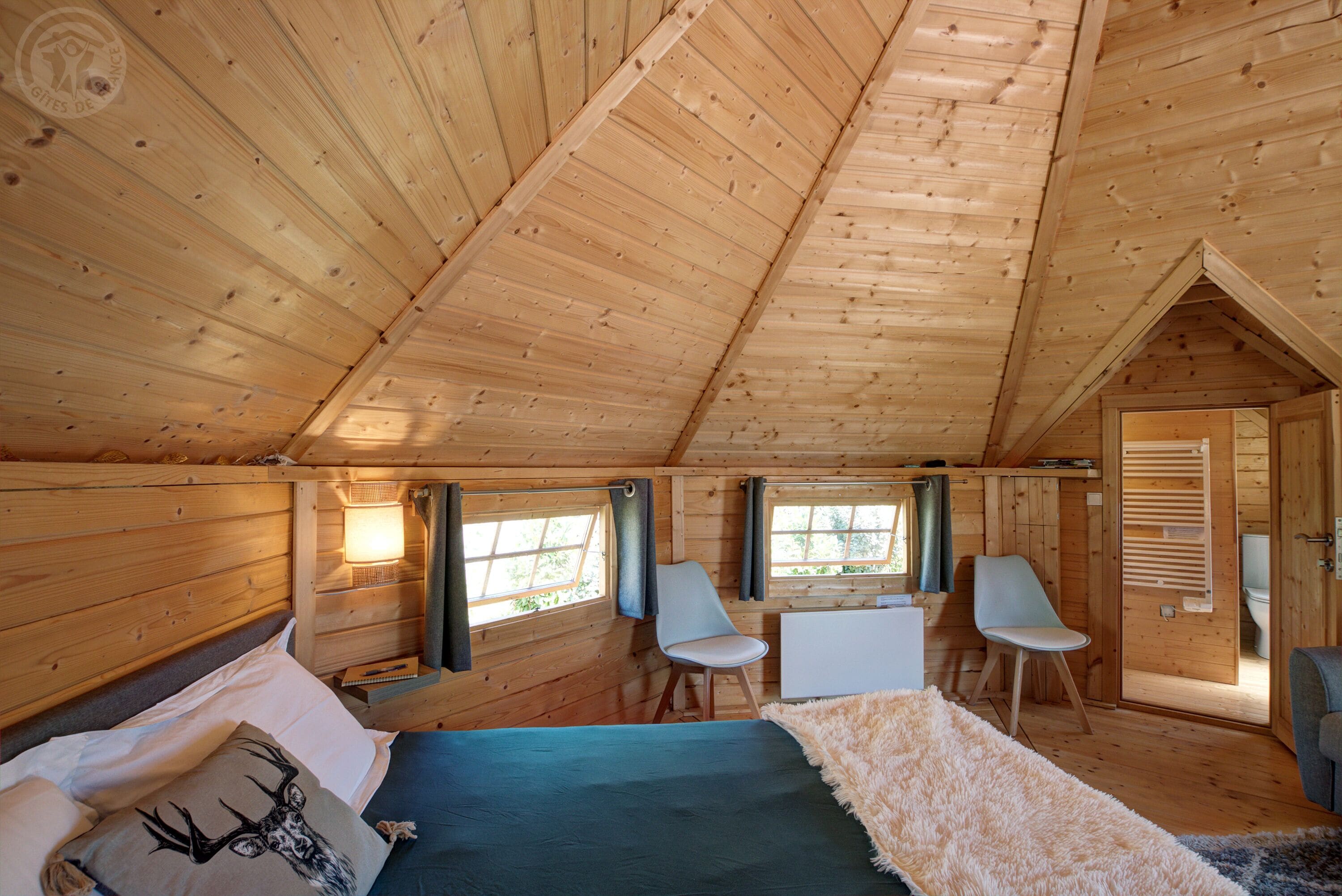 Une chambre confortable, aménagée dans un chalet en bois, avec un lit, deux chaises, un bureau et une fenêtre.