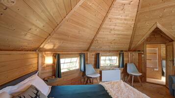 Une chambre confortable, aménagée dans un chalet en bois, avec un lit, deux chaises, un bureau et une fenêtre.