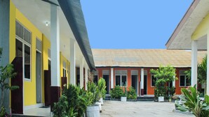 A courtyard with a yellow building, a red building, and potted plants. - Hotel O Wisma Harapan Baik (Kupang)