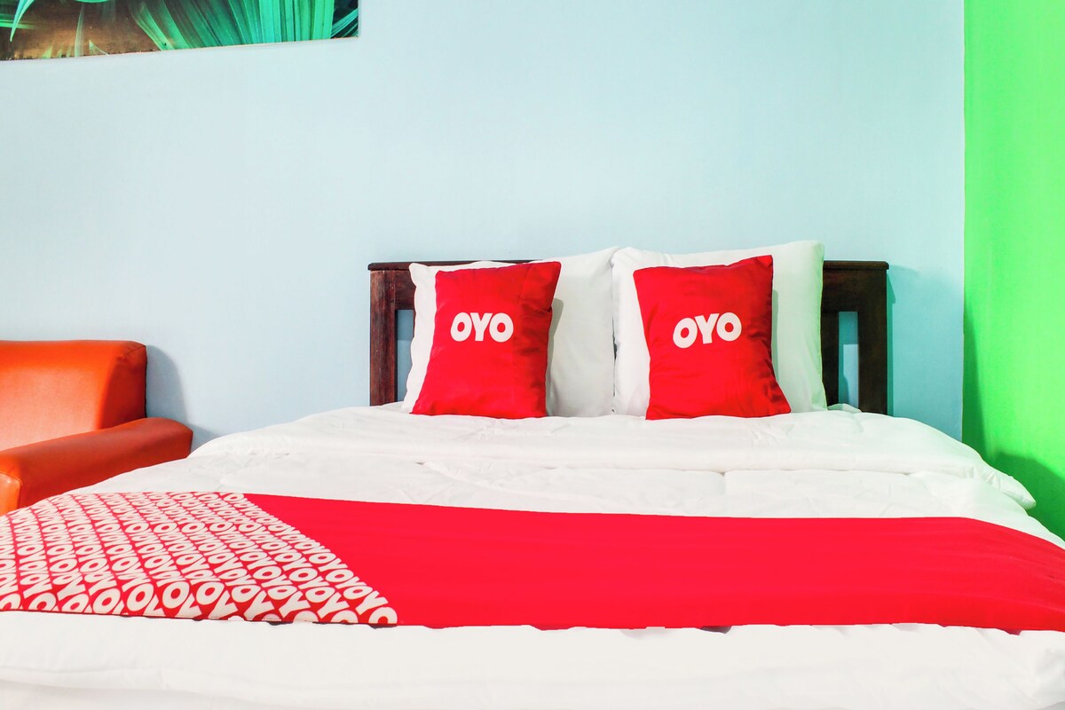 Un lit avec une literie rouge et blanche, deux oreillers rouges ornés du mot « OYO », une couverture rouge et blanche à motifs et une tête de lit en bois.