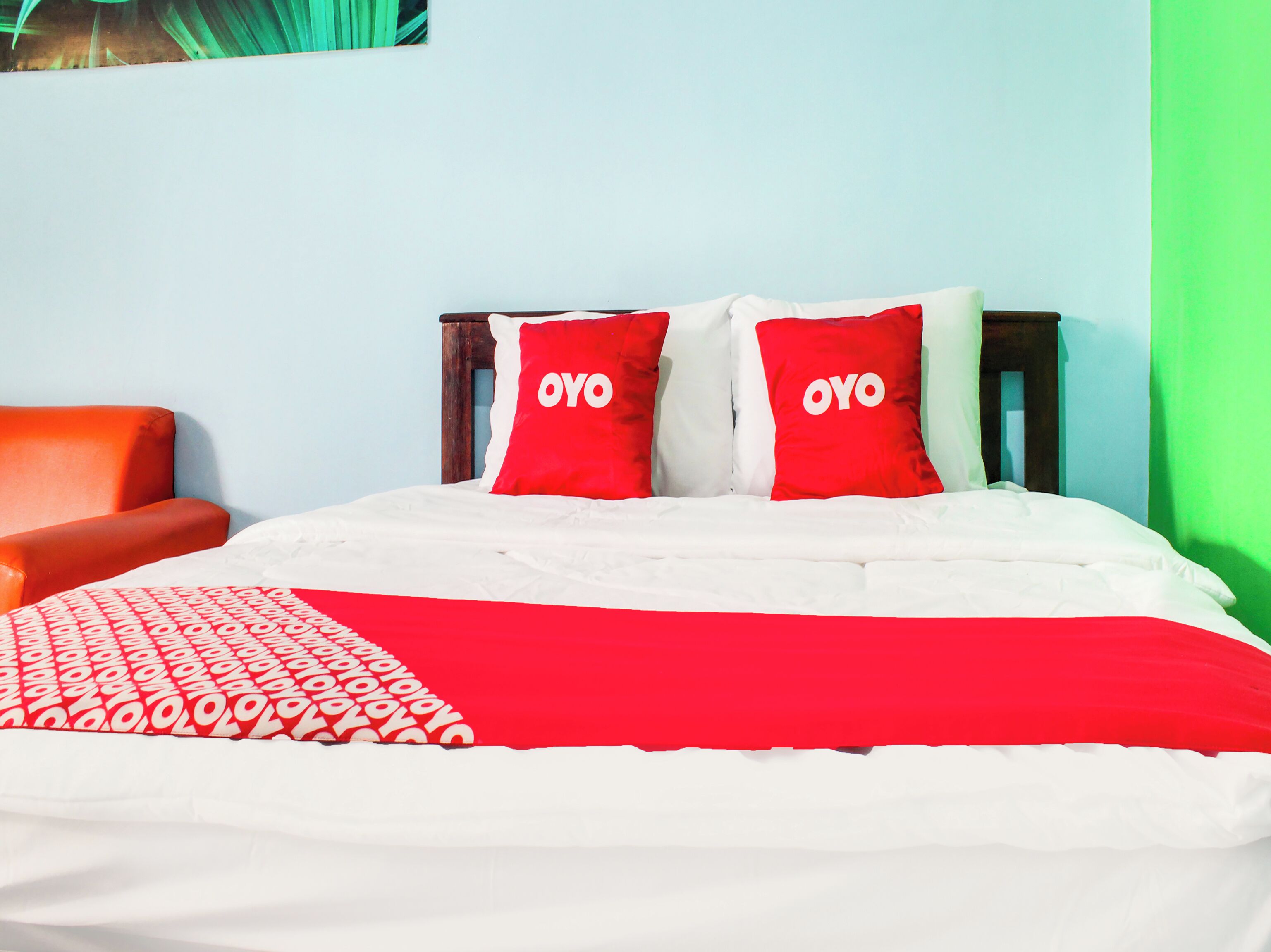 Una cama con ropa de cama roja y blanca, dos almohadas rojas con el texto 'OYO', una manta estampada en rojo y blanco, y un cabecero de madera.