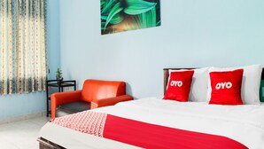 A hotel room with a bed, a red and white patterned bedspread, a red chair, and a curtain with a floral pattern. - Hotel O Wisma Harapan Baik (Kupang)