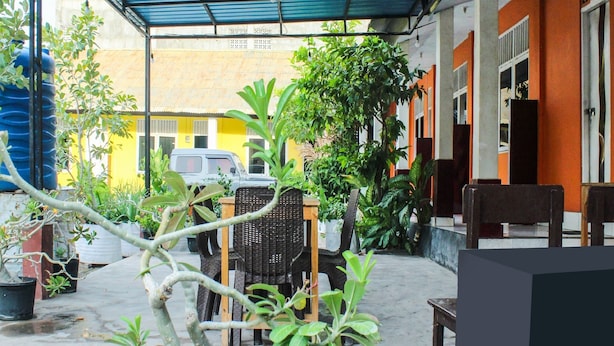 An outdoor patio area with a covered seating area, potted plants, and a parked vehicle. - Hotel O Wisma Harapan Baik (Kupang)