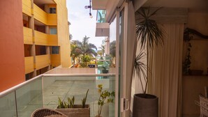 A balcony with a wicker chair, potted plants, and a view of a yellow building and palm trees. - 2BDR Apt Specially designed Morros 922. Host:ID+10 (Cartagena de Indias)