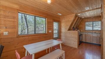 Una cabaña de madera con comedor, cocina y grandes ventanales que dan a un bosque.