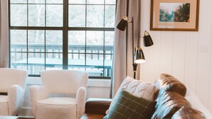 Een gezellige woonkamer met een leren bank, een witte fauteuil en een houten plafond.