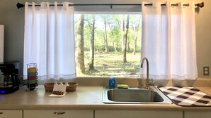 Una cocina con ventana, una cafetera, una taza, una botella de detergente para platos y un mantel a cuadros.