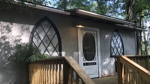 Una terraza de madera con una puerta blanca y dos ventanas arqueadas.
