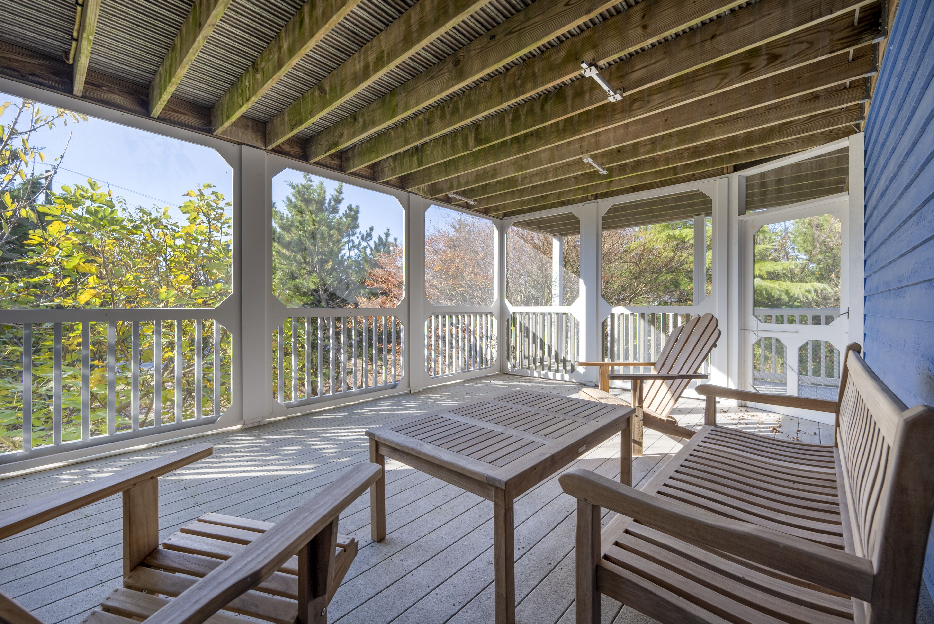 A wooden deck with benches and a table, surrounded by white railings and covered by a wooden roof.
