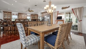 A spacious dining area with a wooden table and chairs, a chandelier, and a large window with curtains. - 8 Lighthouse Way - Beautiful home with a private elevator! (Lewes)