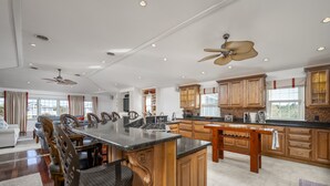 A spacious kitchen with wooden cabinets, a large island, and a dining area with chairs and a table. - 8 Lighthouse Way - Beautiful home with a private elevator! (Lewes)