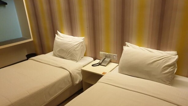 A hotel room with two single beds, a bedside table with a phone, and a striped curtain in the background.